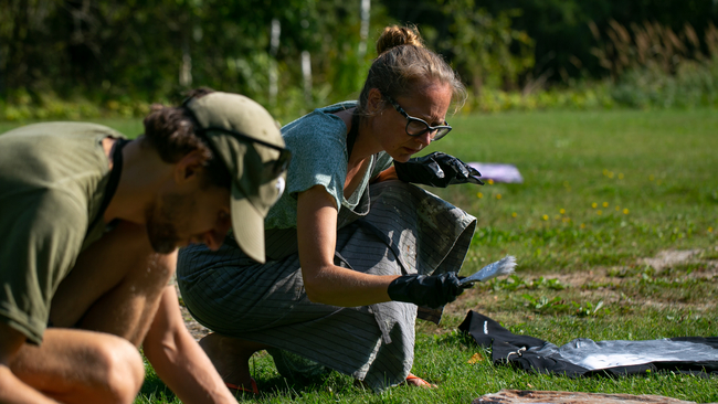Outside workshop where two people are sitting on grass and painting clothes.