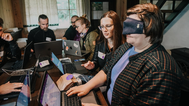 Blindfolded person typing on a computer while other person is giving instructions.
