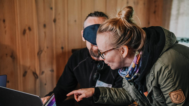 Blindfolded person typing on a computer while other person is giving instructions
