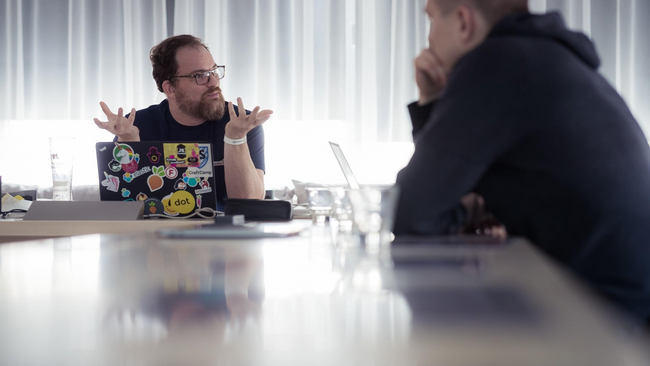Two people sitting at the table laptops open and conversing.