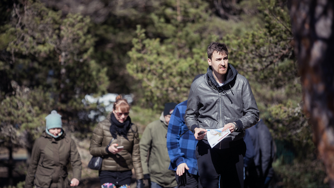 Group of people outside following a person with an orienteering map.
