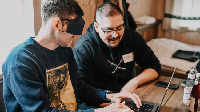 A person showing a blindfolded person how to operate a keyboard with speech