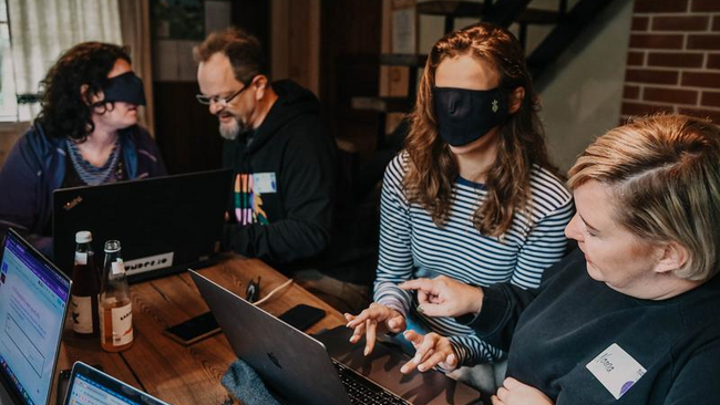 A person assisting another person that has a blindfold to use a computer